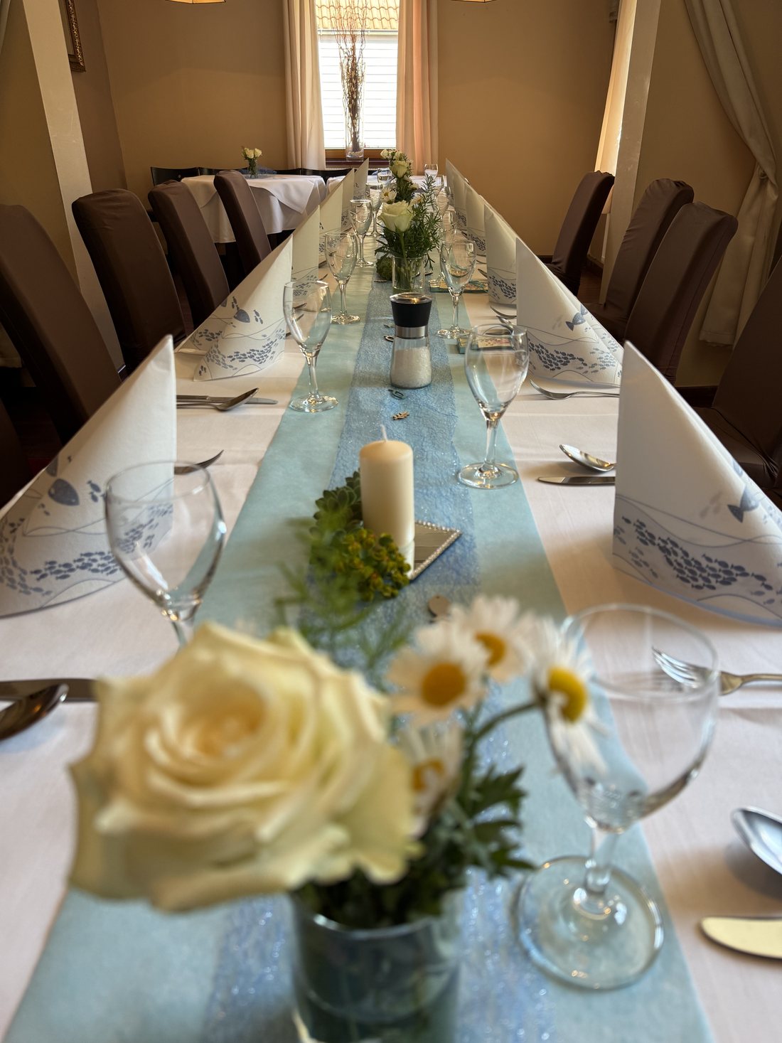 Festlich gedeckte Tafel mit blauem Tischläufer, Kerze und Blumen zur Erstkommunion